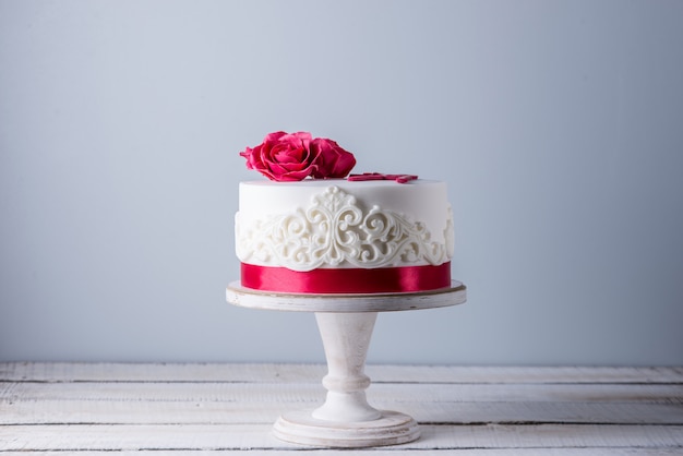 Beautiful white wedding cake decorated with flowers red roses and ribbon