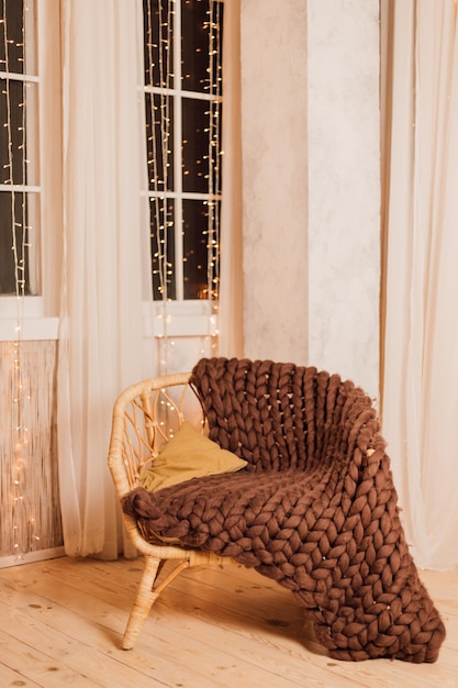 A beautiful wicker chair covered with a knitted bedspread stands near the wall with a window