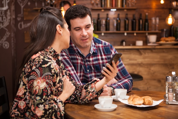 La bella moglie e il marito guardano il telefono mentre cenano. pub alla moda.