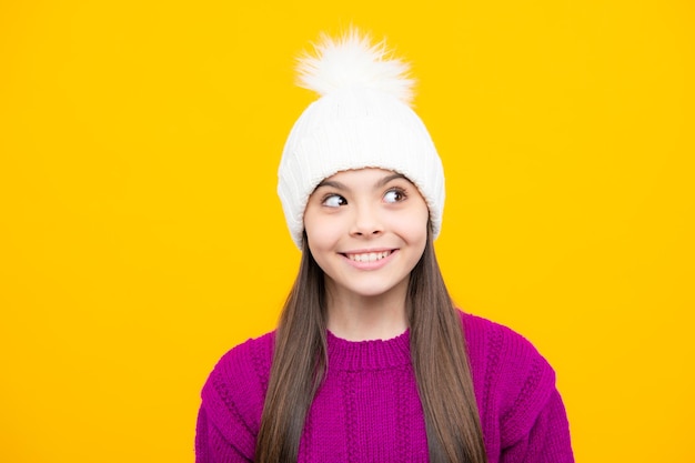 冬のセーターと黄色の背景にニット帽子でポーズ美しい冬の子供の肖像画ティーンエイ ジャーの女の子