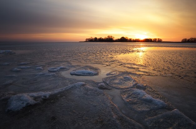 Beautiful winter landscape with sunset fiery sky and frozen lake. Composition of nature.