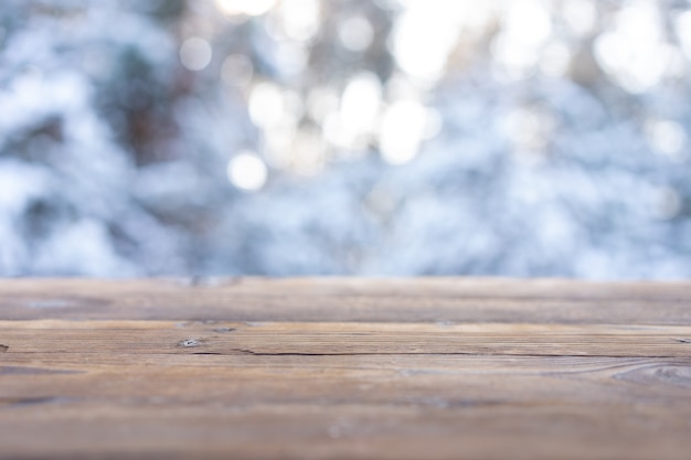 美しい冬のシーン。雪に覆われたクリスマスの自然の背景のぼやけた背景、光沢のあるボケ味の木製テーブルトップ。製品展示用クリスマスタイムモックアップ