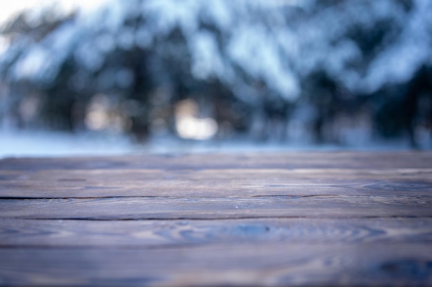 美しい冬のシーン。雪に覆われたクリスマスの自然の背景のぼやけた背景、光沢のあるボケ味の木製テーブルトップ。製品展示用クリスマスタイムモックアップ