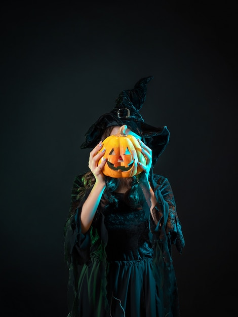 Photo beautiful witch in a pointed hat holding a pumpkin with a laughing face,