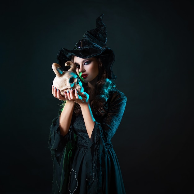 Beautiful witch in a pointed hat holds a the demons skull in her hands