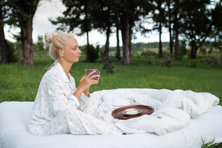 Photo beautiful woman 22-24 year old sitting in bed on white blanket drinking coffee outdoors over nature