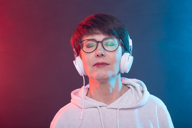 Beautiful woman 40-50 years old listening music in big headphone on blue background.