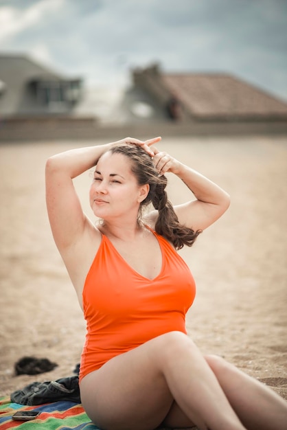 Beautiful woman 40 years old plus size, on the beach in an orange swimsuit, body positivity theme