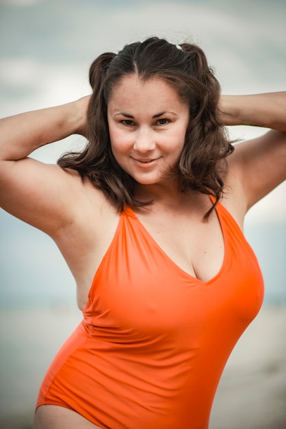 Beautiful woman 40 years old plus size, on the beach in an orange swimsuit, body positivity theme