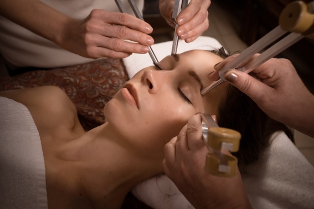Beautiful woman during antiage face sound massage acutonics session with tuning forks