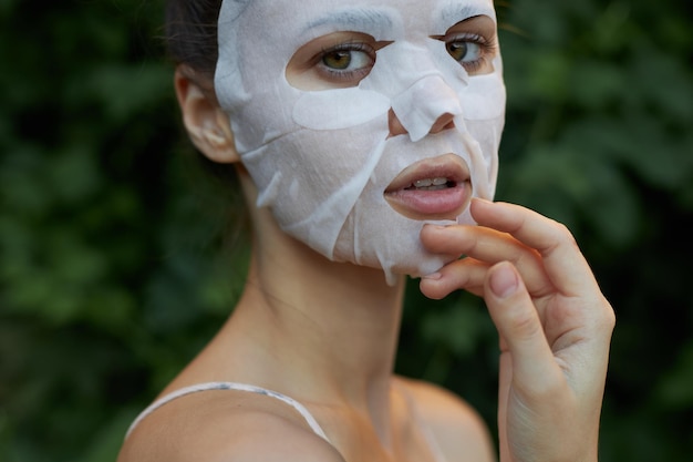 Beautiful woman Antiwrinkle mask Touch your face with your hand skin care leaves in the background