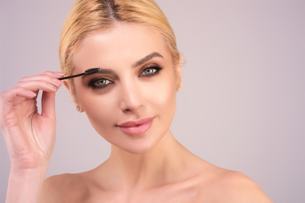 Beautiful woman applies brow gel with brows brush to her eyebrow studio portrait of young woman doin