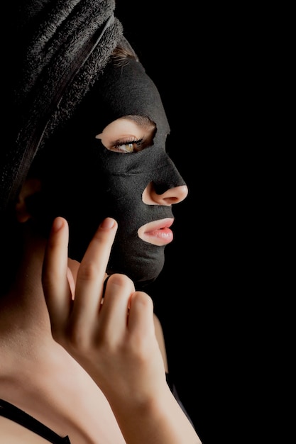 Beautiful woman applying black facial mask. beauty treatments.
close-up portrait of spa girl apply clay facial mask on black