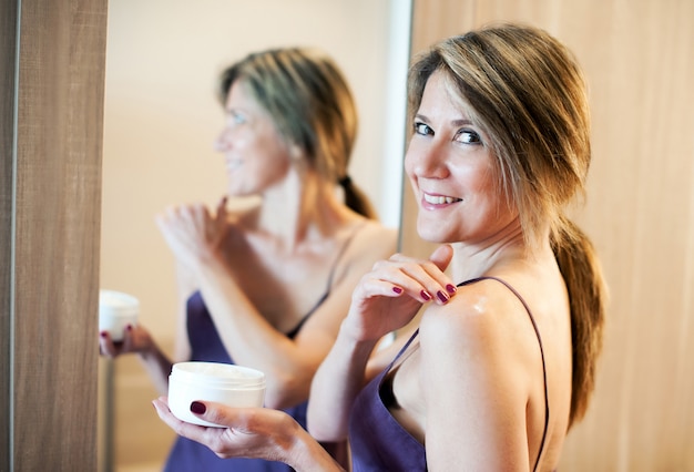 Beautiful woman applying cream on shoulder