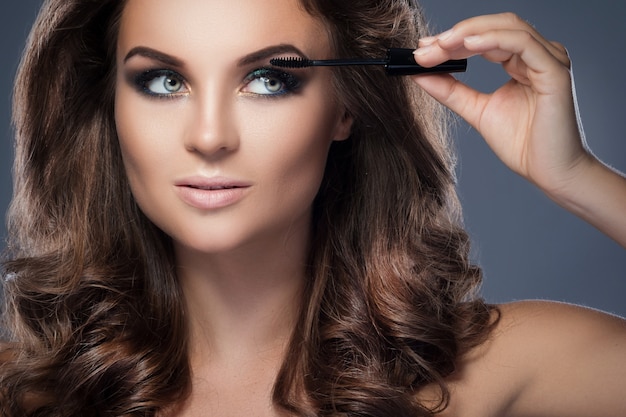 Beautiful woman applying mascara on her lashes