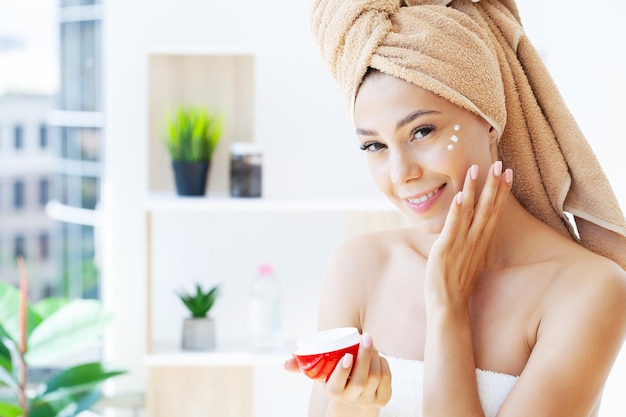 Beautiful woman applying moisturizer cream on her face