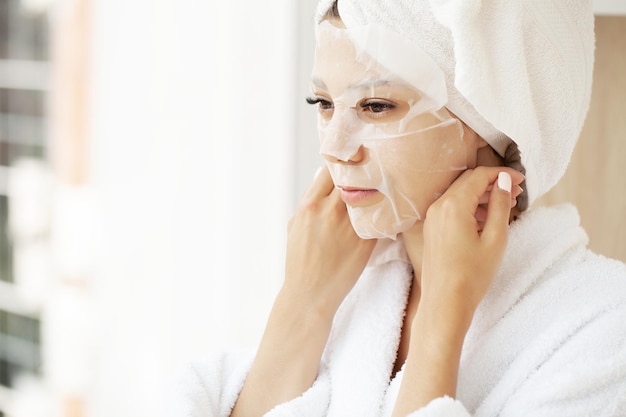 Beautiful woman applying paper sheet mask on her face white