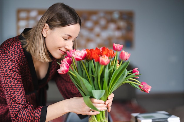 Beautiful woman arranging flowers presented by her husbant at home happy and joyful