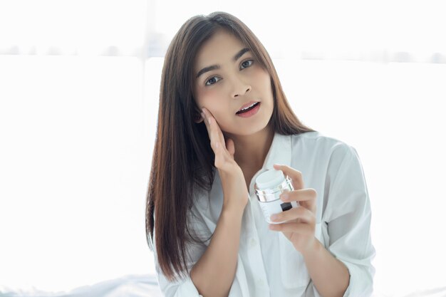 A beautiful woman asian using a skin care product, moisturizer or lotion taking care of her dry complexion. Moisturizing cream in female hands .