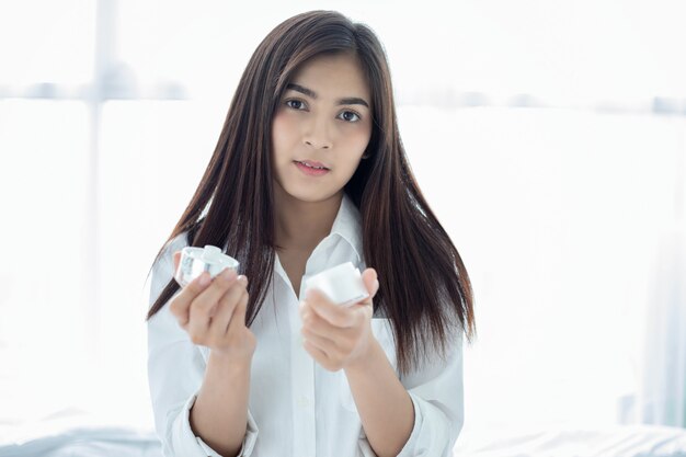 A beautiful woman asian using a skin care product, moisturizer or lotion taking care of her dry complexion. Moisturizing cream in female hands .