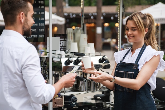 Bella donna barista che vende caffè al cliente nel caffè di strada