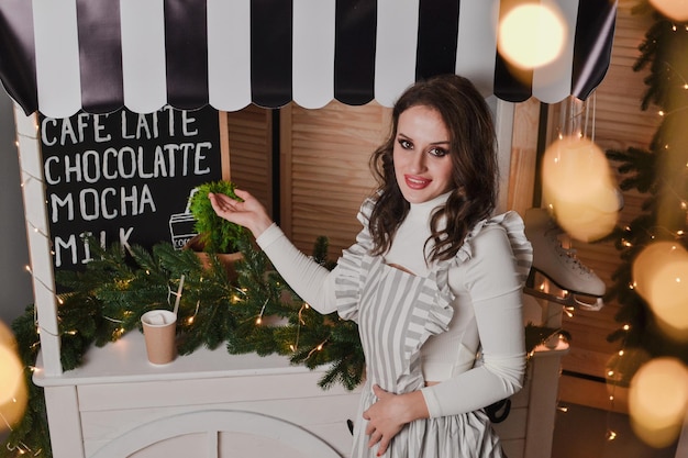 beautiful woman barista in striped apron holds coffee cup in hand New year showcase