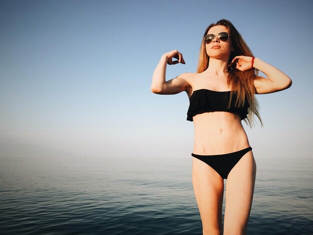 Photo beautiful woman in bikini standing at beach against clear sky on sunny day