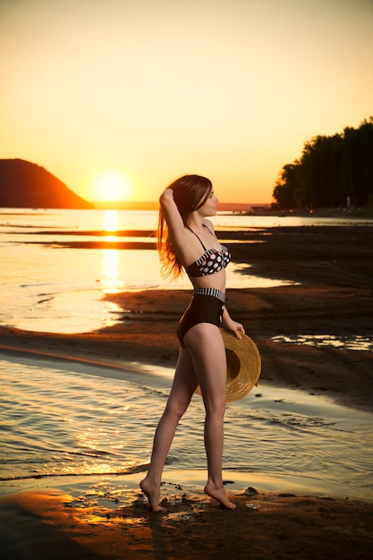 Bella donna in bikini su sfondo tramonto. ragazza esile che posa in un costume da bagno