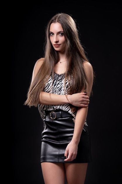 Beautiful woman on black background in leather skirt and patterned shirt