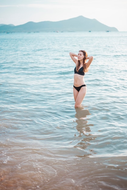 黒のビキニを着た美しい女性がビーチで海水を楽しんでいます。