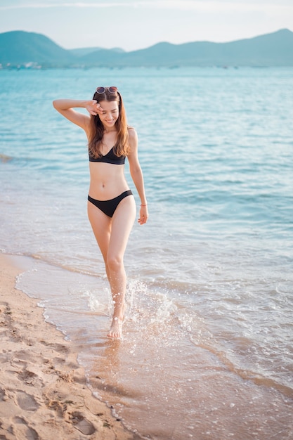 Beautiful woman in black bikini is walking from sea, summer concept 