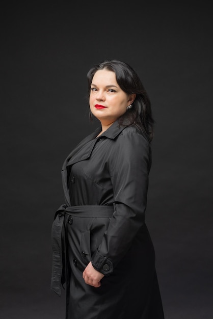 A beautiful woman in a black coat stands on a black background