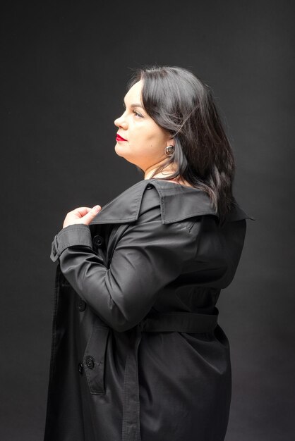 A beautiful woman in a black coat stands on a black background