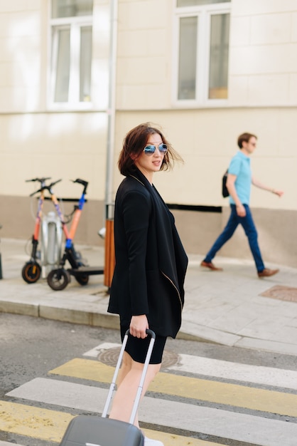 Beautiful woman in black dress on a background of an urban landscape with a suitcase