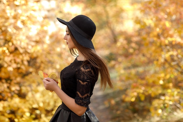 Beautiful woman in black dress and hat in autumn