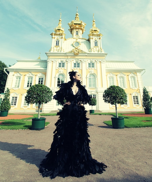 Beautiful woman in black dress posing next to the palace. Dark Queen.