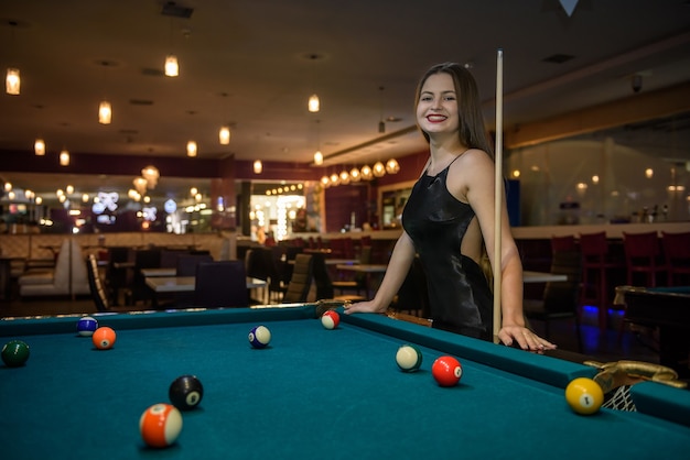 Beautiful woman in black dress posing with billiard cue