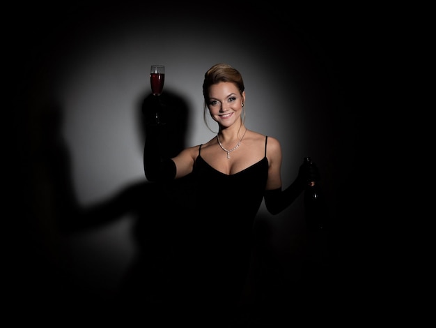 Beautiful woman in a black dress with a neckline and long velvet gloves dancing and holding champagn...