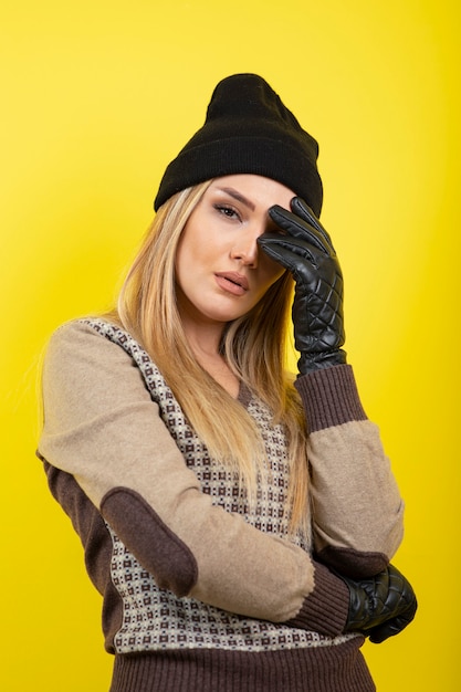 Bella donna in guanti neri e cappello in posa sul giallo.