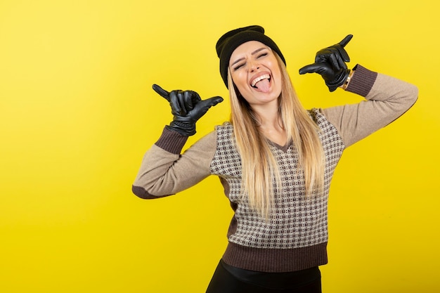 Beautiful woman in black gloves and hat posing on yellow.