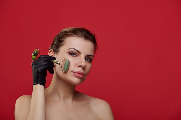 Beautiful woman in black gloves massaging her face with a jade roller