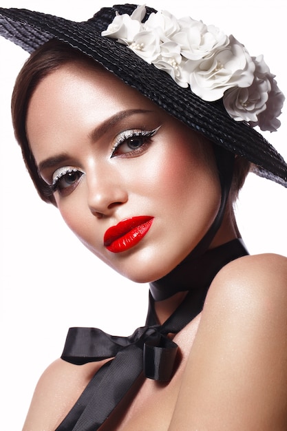 Beautiful woman in a black hat with flowers and retro makeup