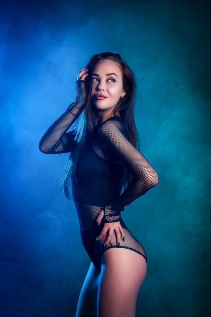 Beautiful woman in black lingerie posing against a blue and pink smoke on a black isolated background