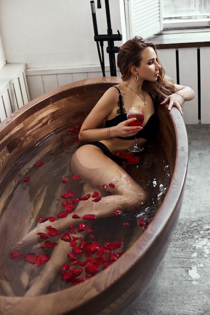 Beautiful woman in black underwear resting in the bathroom. A woman in love rests, flowers and rose petals