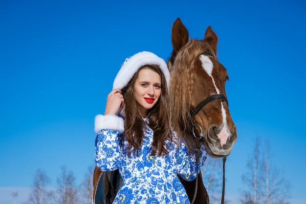 Beautiful woman in a blue coat riding a horse in winter on a Sunny day