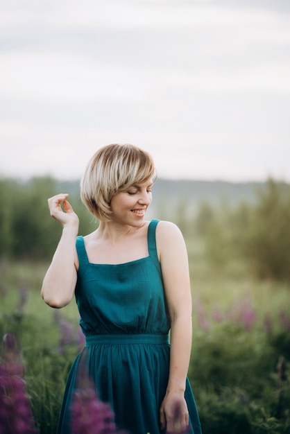 A beautiful woman in a blue dress in a field of lupine flowers dances and smiles.