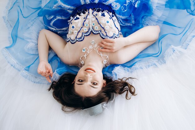 a beautiful woman in a blue evening dress and a small hat lies on the floor