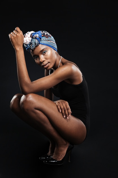 Beautiful woman in bodysuit posing in studio sitting isolated on the black wall