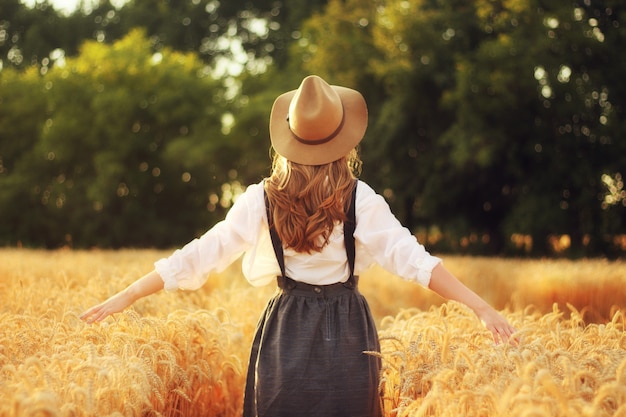 Beautiful woman in brown hat in golden wheat field.