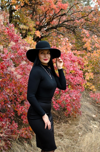 Beautiful woman brunette in a hat in the autumn stands in a park